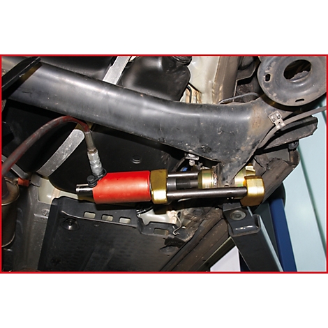 Nahaufnahme des Unterbodens eines Autos mit einer rot-goldenen Werkzeugvorrichtung.